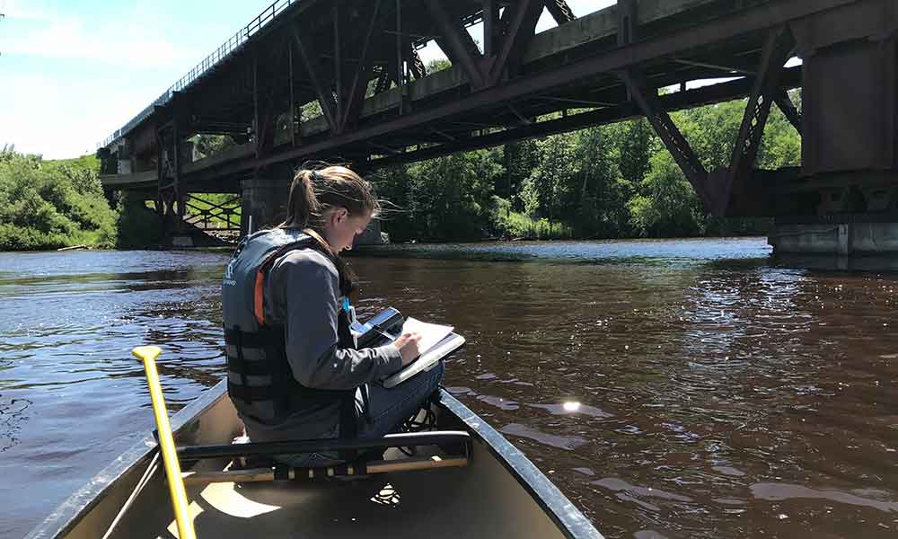 A young woman taking notes while in a canoe on a river
