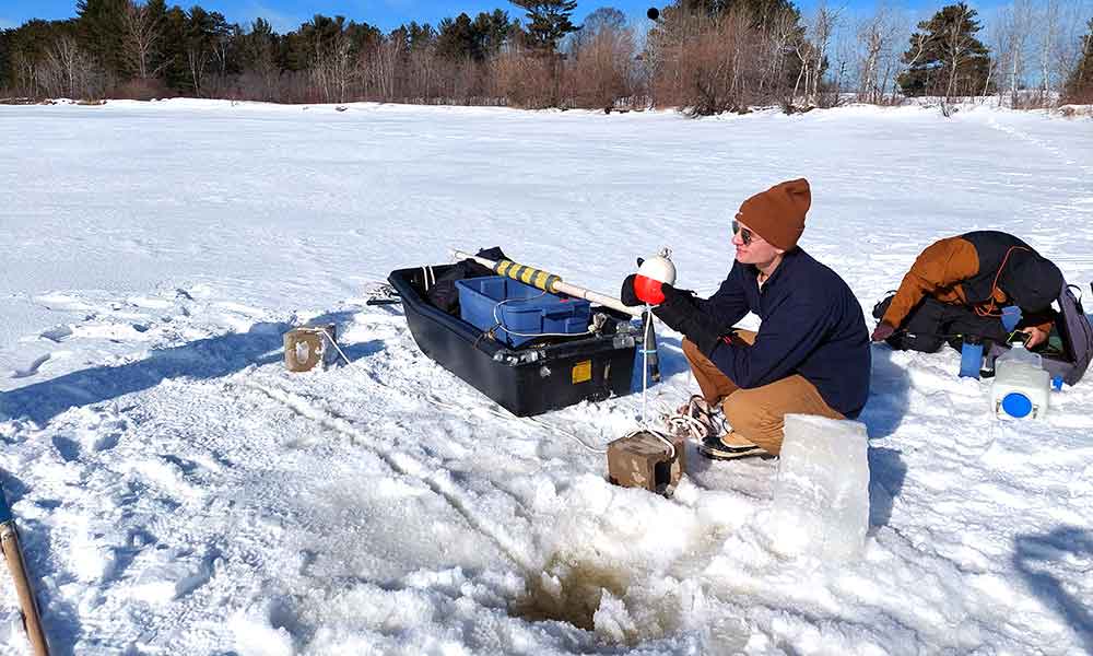 A young man sitting in the snow on a frozen lake. while he collects water samples