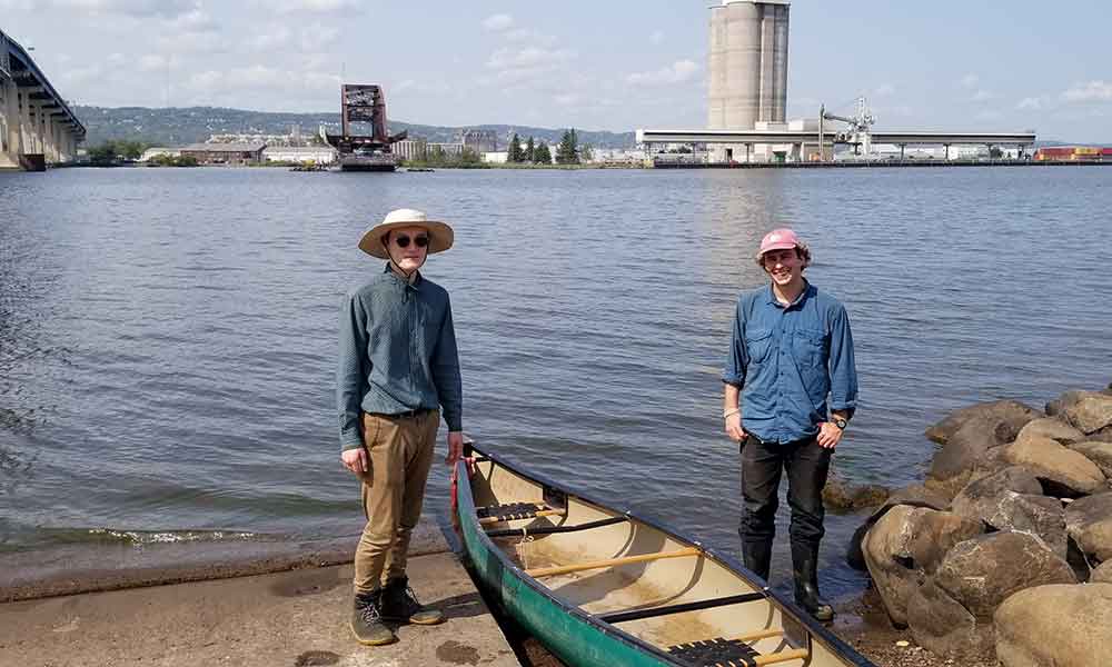 Two young men with a canoe at the edge of a river